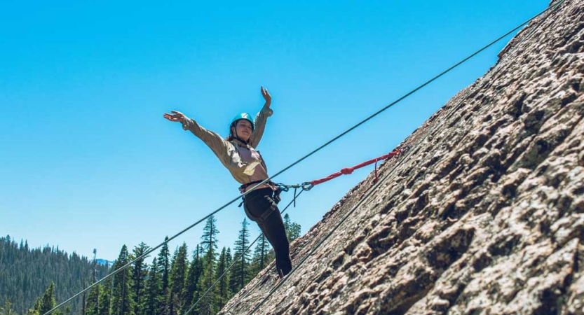 A person wearing safety gear is secured by ropes as they stand on the rocky incline they are climbing. 